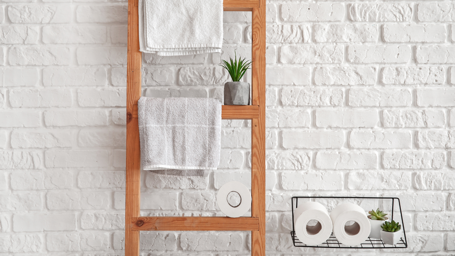 Minimalist bathroom setup with organic toilet paper rolls, white towels, and small potted plants against a white brick wall.