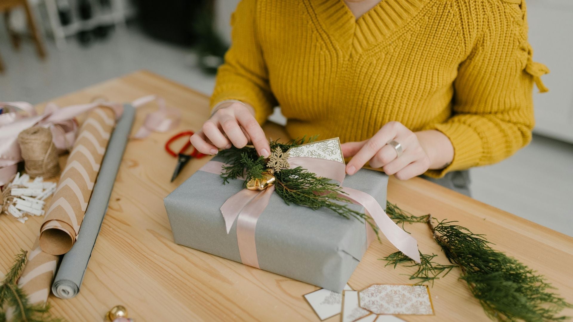 Woman wrapping an eco-friendly holiday gift with reusable ribbon, fresh greenery, and plastic-free decor on a wooden table