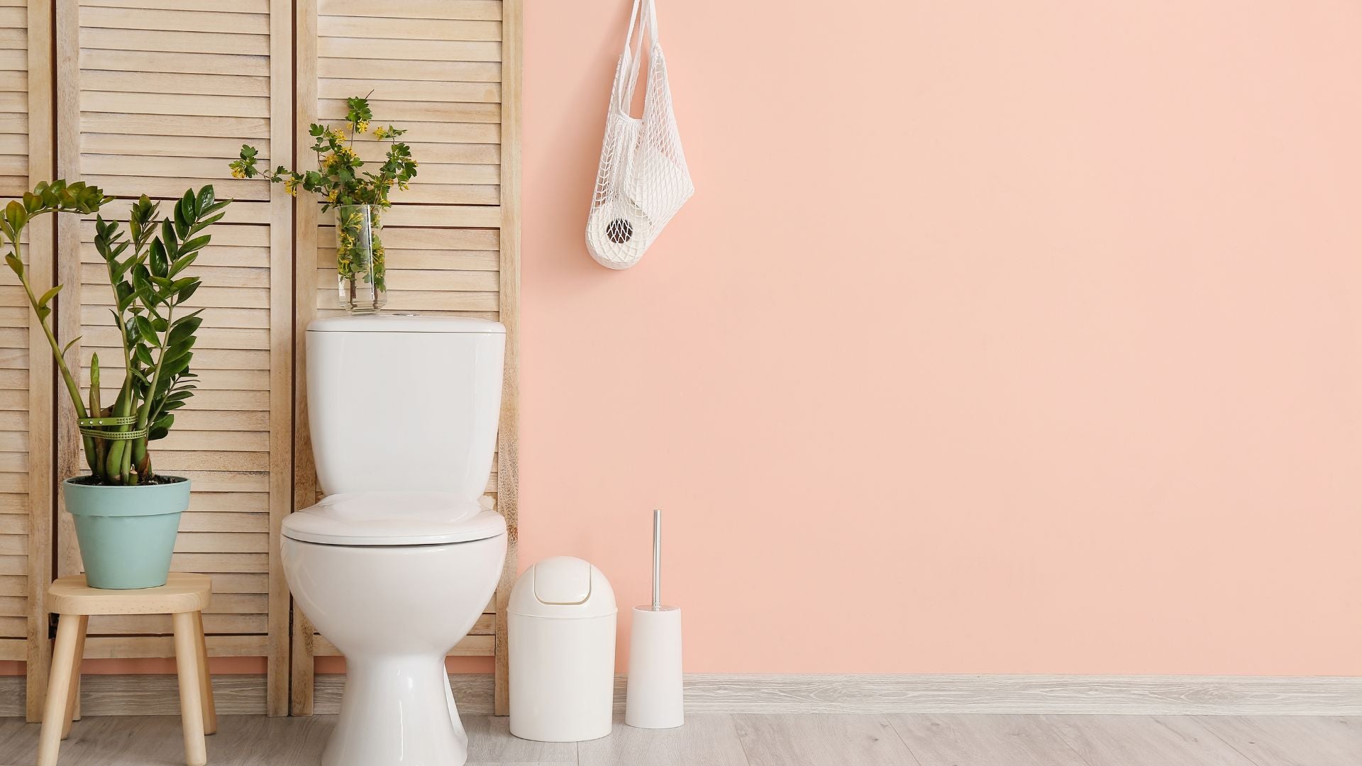 Minimalist bathroom with indoor plants and eco-friendly accessories, including a hanging mesh bag holding bamboo toilet paper — styled for sustainability and wellness.