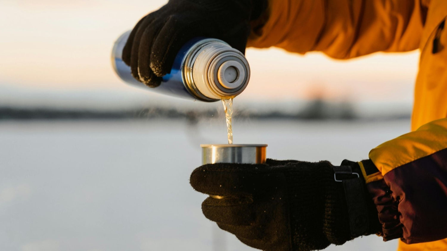 Gloved hands pouring hot beverage from a thermos into a cup outdoors on a snowy day—highlighting low-waste, reusable travel gear for winter adventures