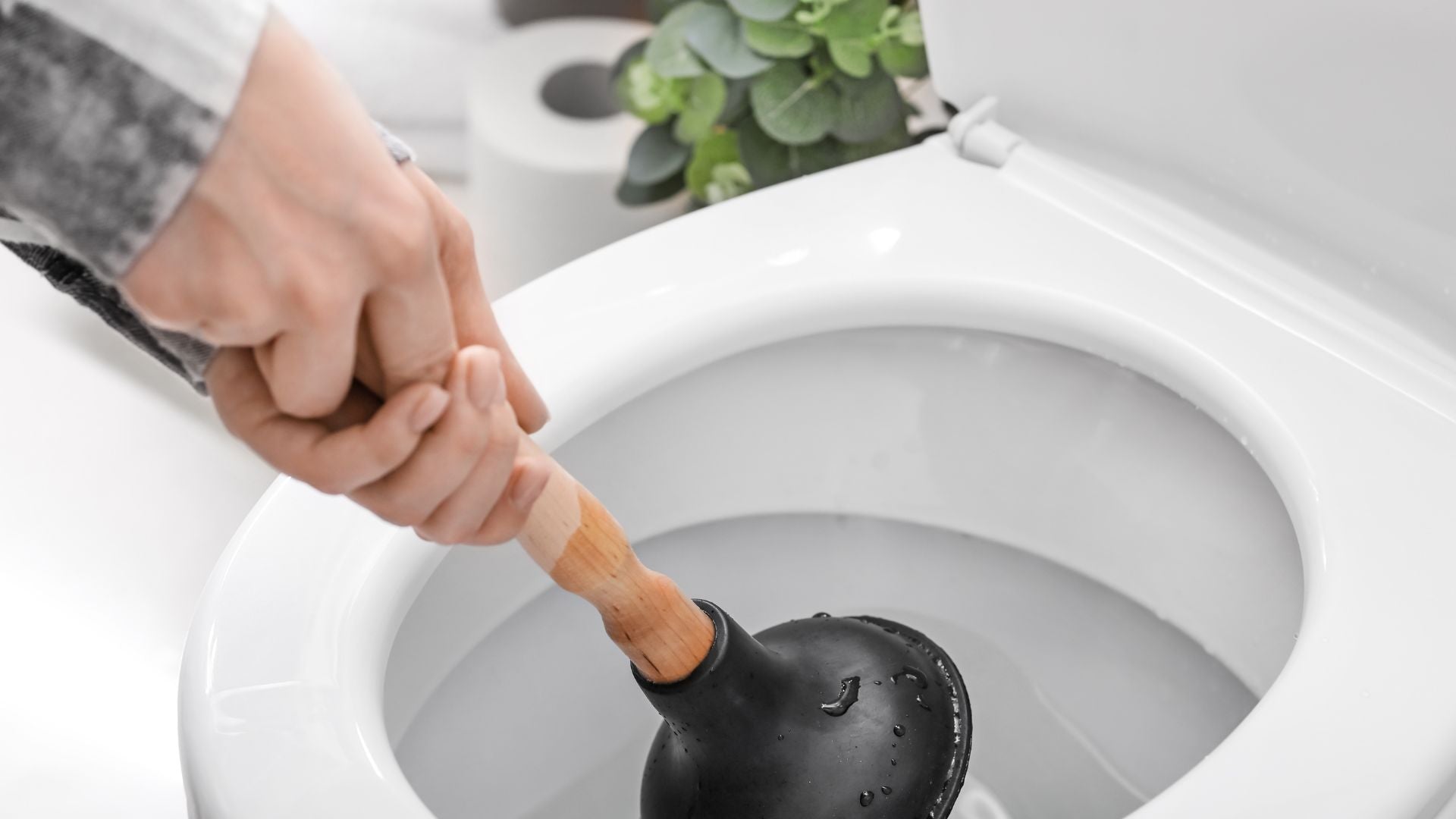 Person unclogging toilet with plunger, emphasizing the need for septic-safe, clog-free toilet paper like ecoHiny bamboo rolls